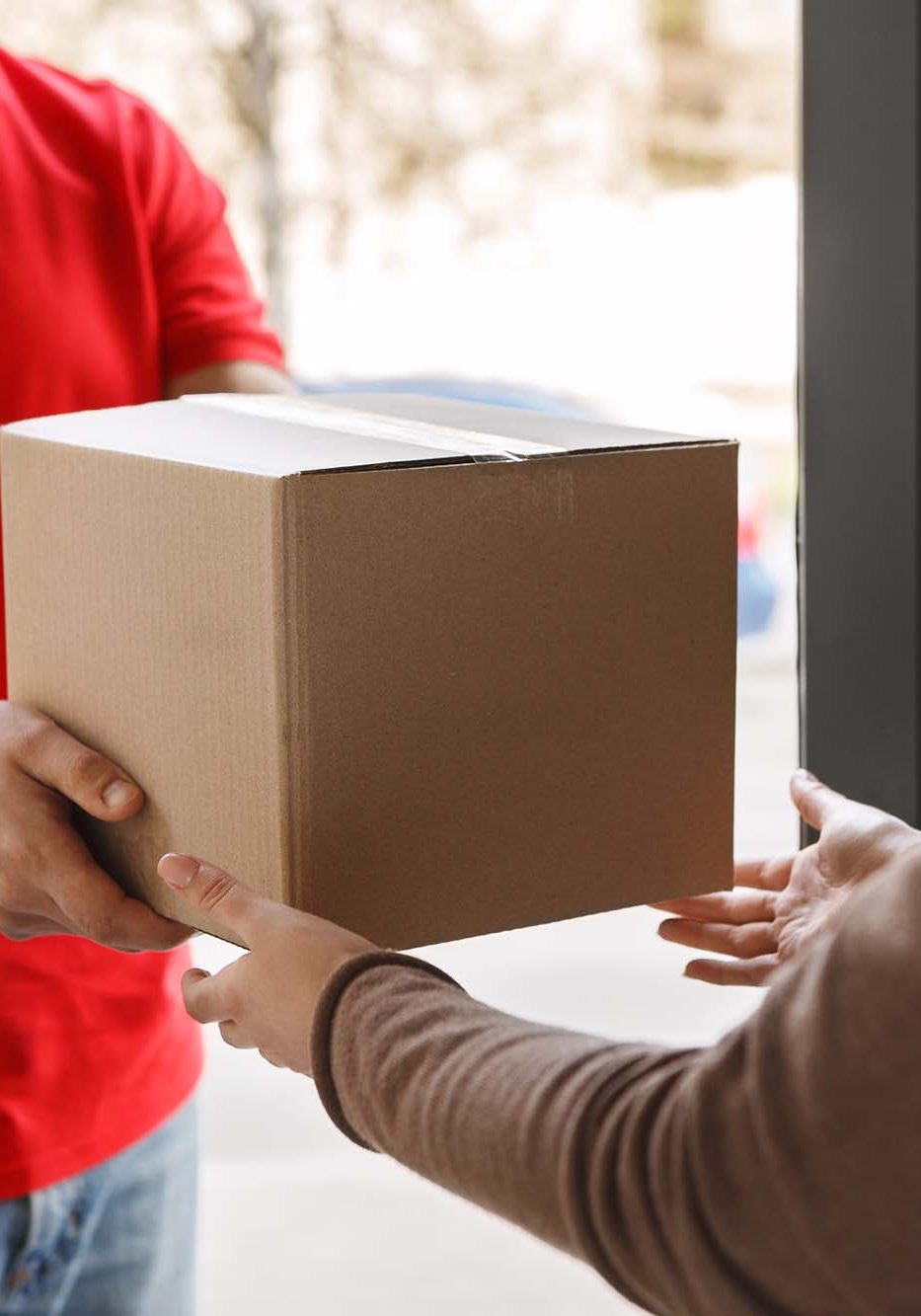 Delivery of parcel from courier to client at home. Deliveryman in red uniform gives box to girl, free space