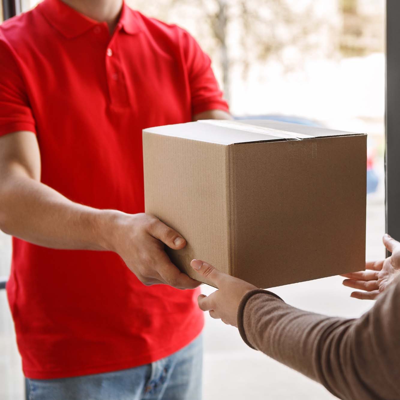 Delivery of parcel from courier to client at home. Deliveryman in red uniform gives box to girl, free space, cropped