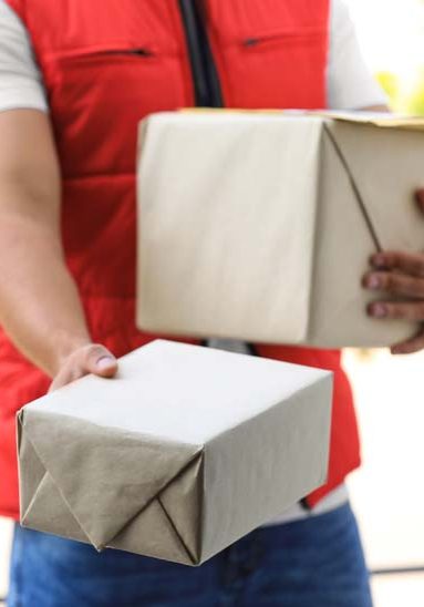 Young courier holding parcels on doorstep, closeup. Delivery service